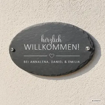 Ovales Willkommensschild „Herzgruß“ aus Schiefer, an der Hauswand mit Edelstahl-Abstandshaltern