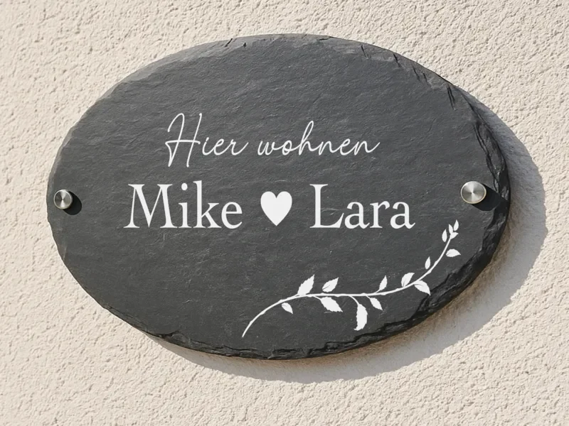 Ovales Türschild aus Schiefer mit „Hier wohnen Mike und Lara“ an einer hellen Wand